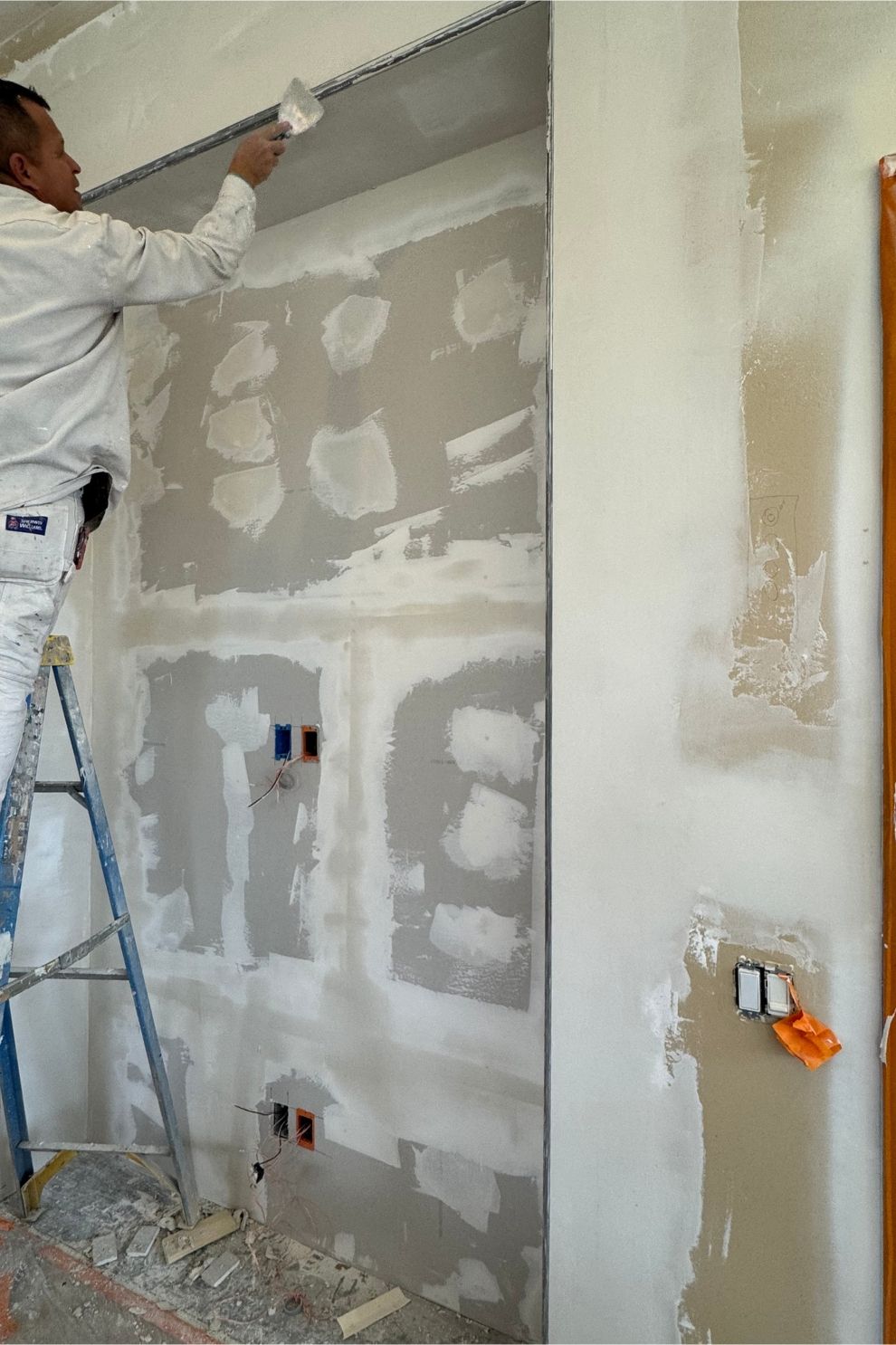 A man is standing on a ladder painting a wall.