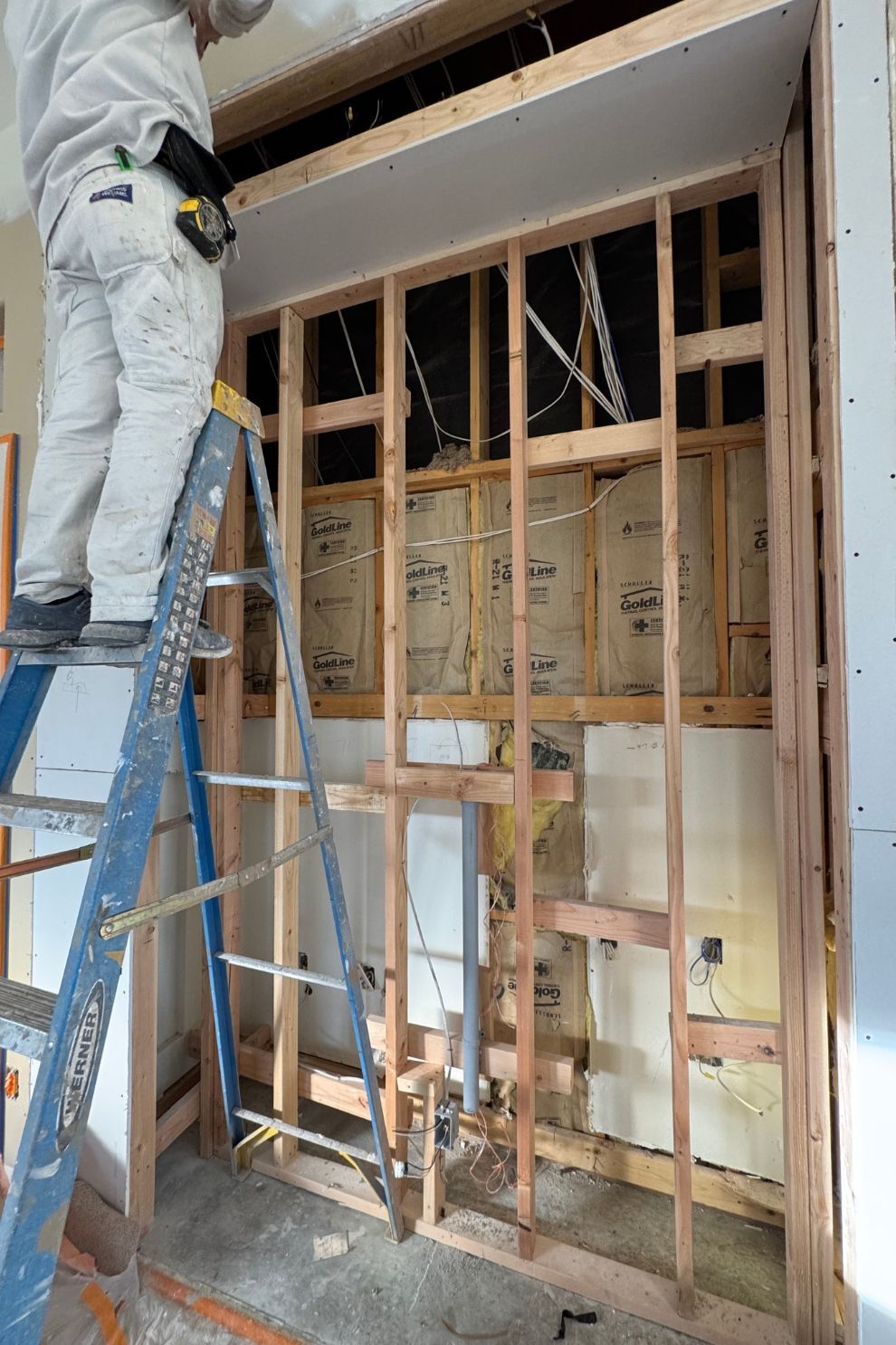A man is standing on a ladder in a room under construction.