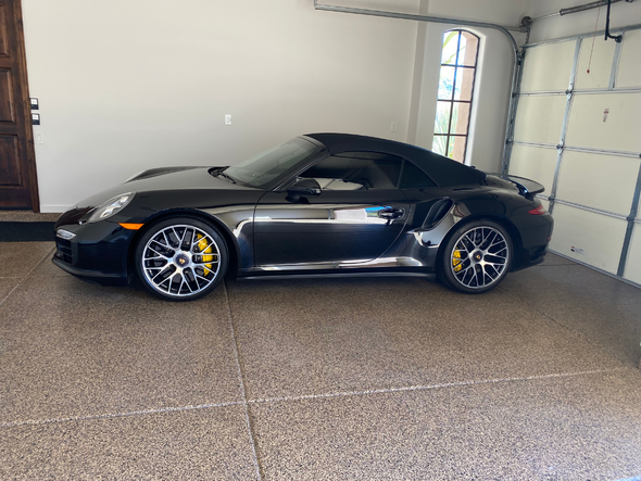 A black porsche 911 turbo convertible is parked in a garage.