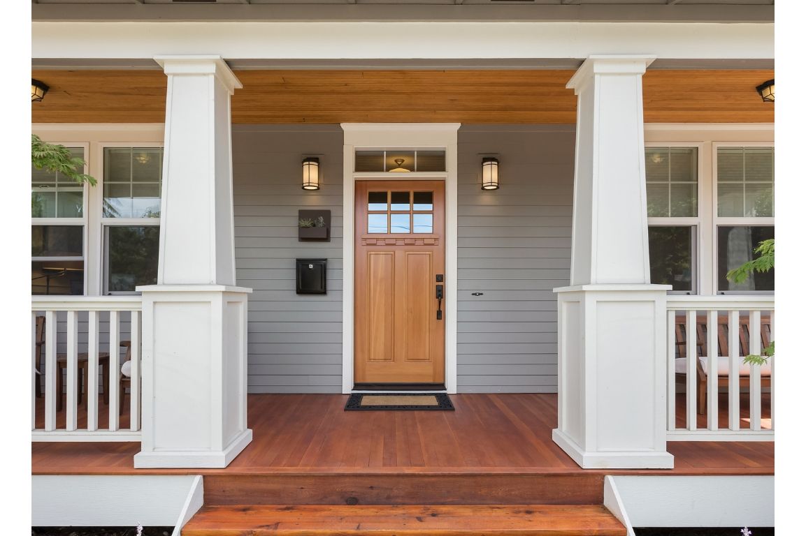 The front porch of a house with a wooden door and steps.