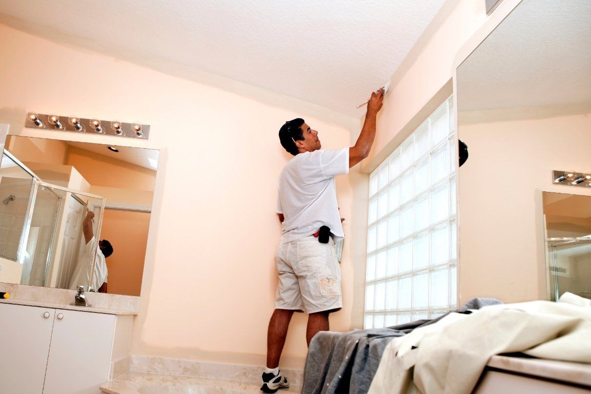 A man is painting a wall in a bathroom.