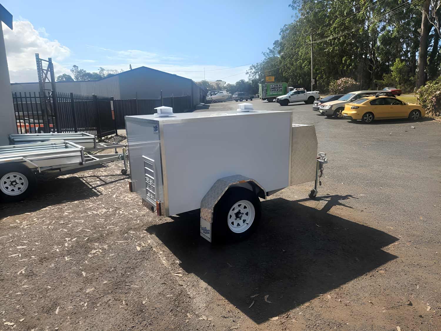 A white trailer is parked in a parking lot next to a yellow car Hastings Trailer Centre in Port Macquarie, NSW