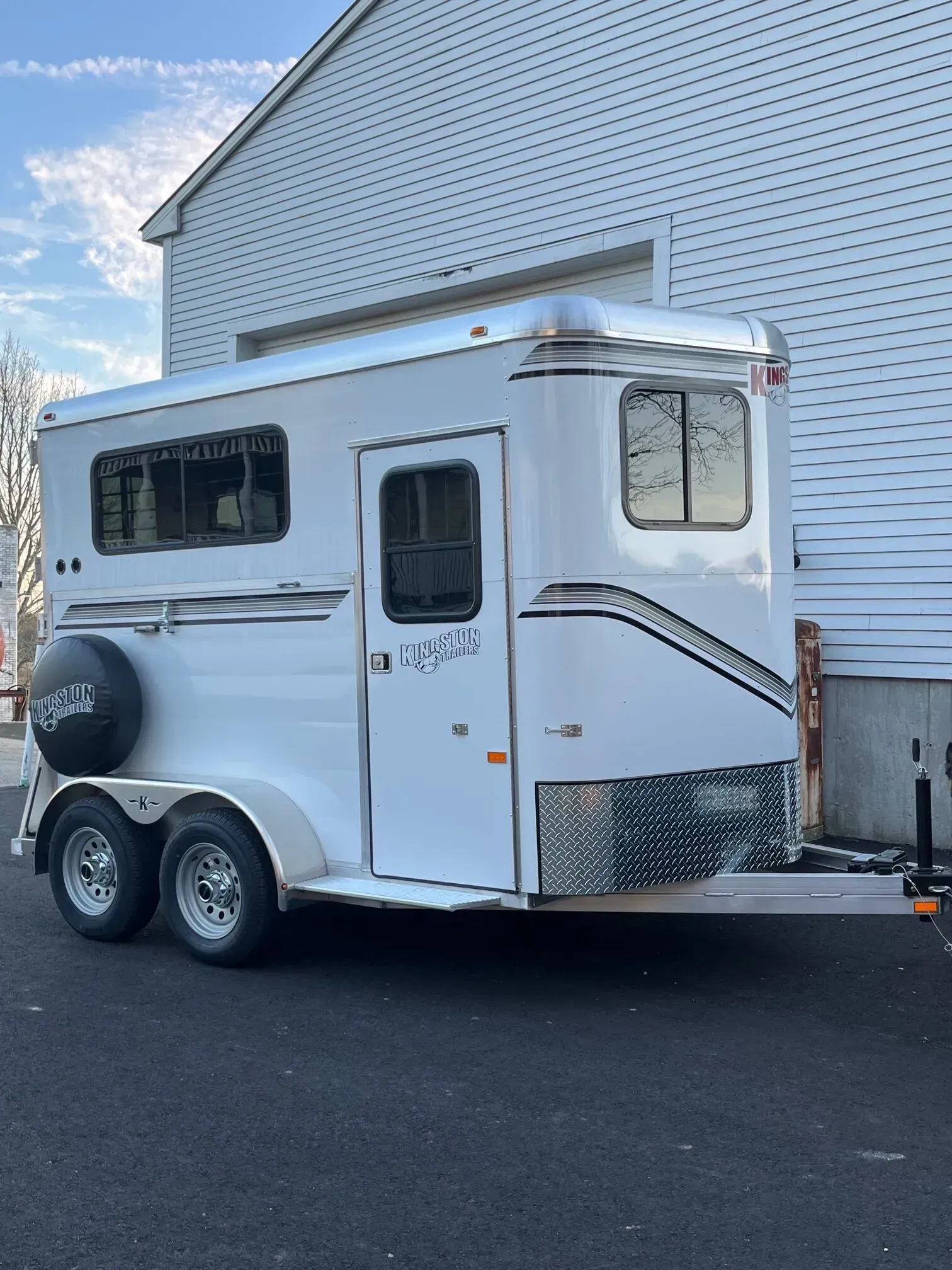 White two-axle horse trailer parked beside a white house on a paved driveway