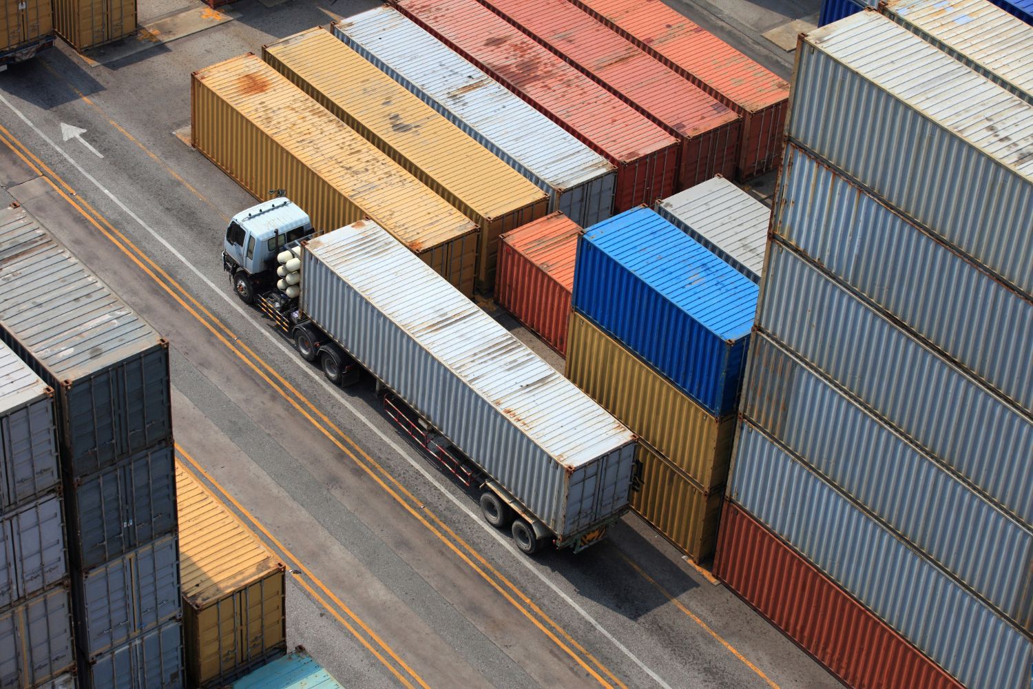 An aerial view of a truck driving past a row of shipping containers.