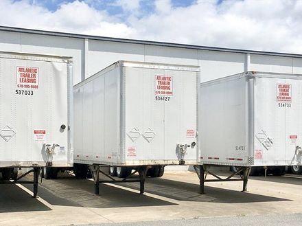 Three white trailers are parked next to each other in a parking lot.