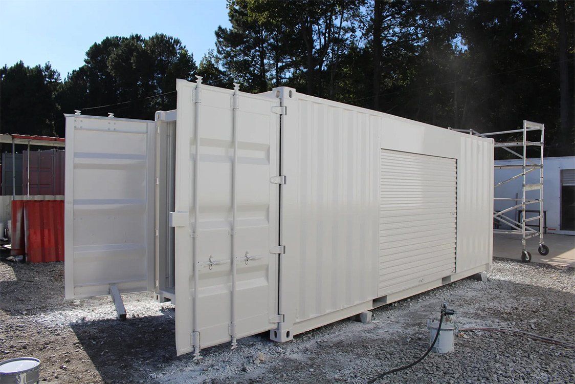 A large white shipping container is sitting on top of a gravel lot.