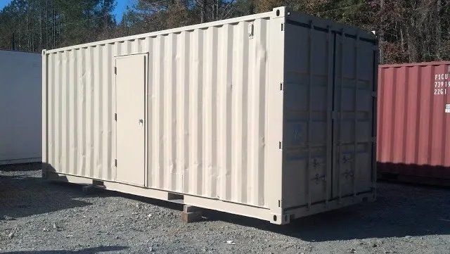 A shipping container with a door is sitting in a gravel lot.