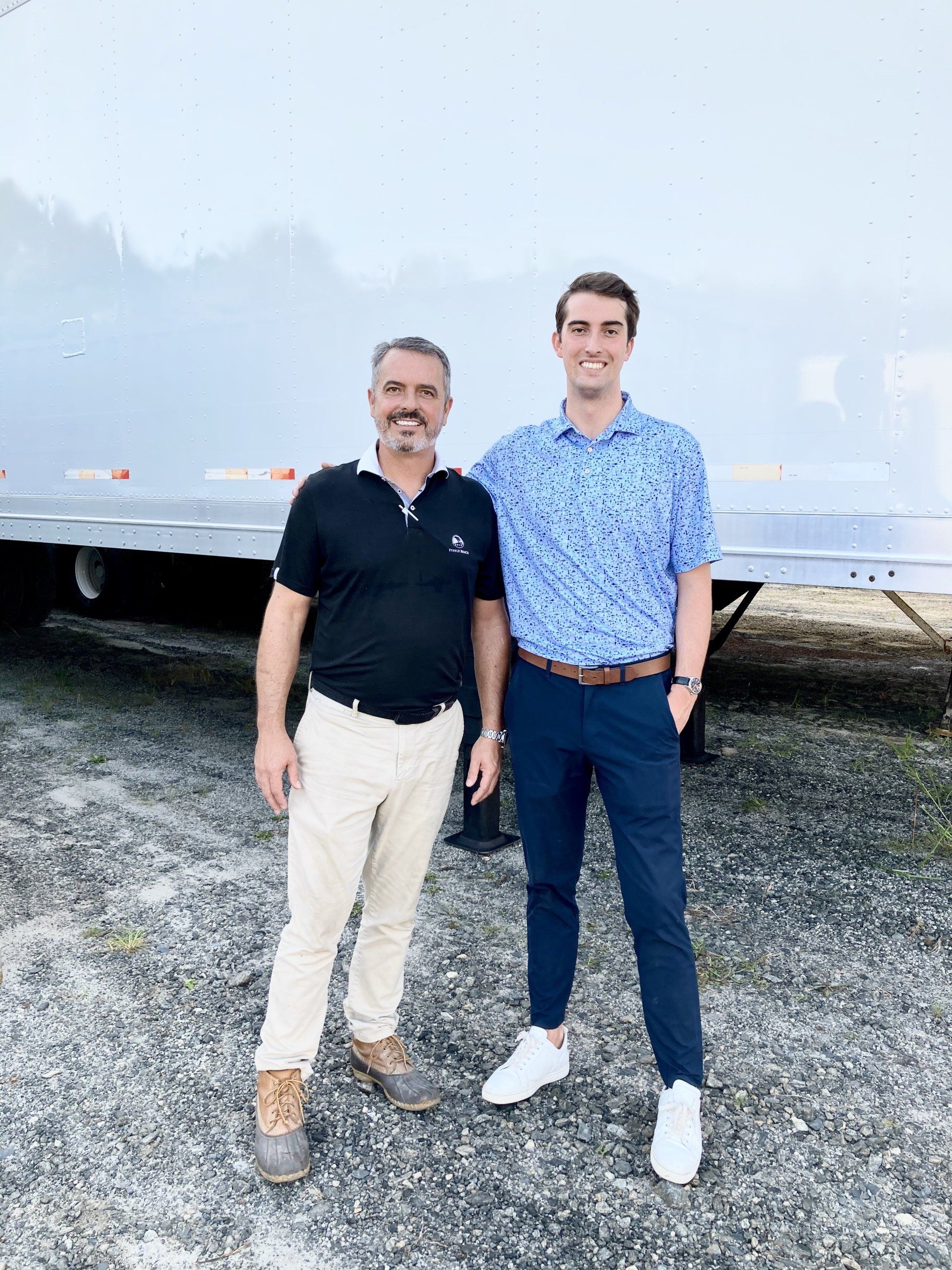 Two men are standing next to each other in front of a trailer.