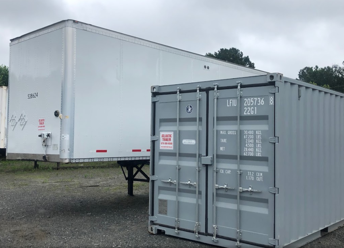 A white trailer is parked next to a gray shipping container.