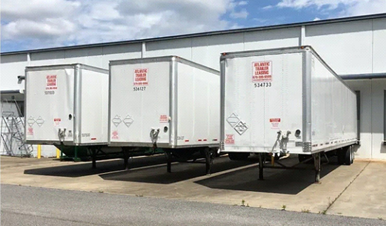 Three white trailers are parked in front of a building.