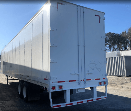 A white trailer with the letter l on the back is parked in a parking lot.