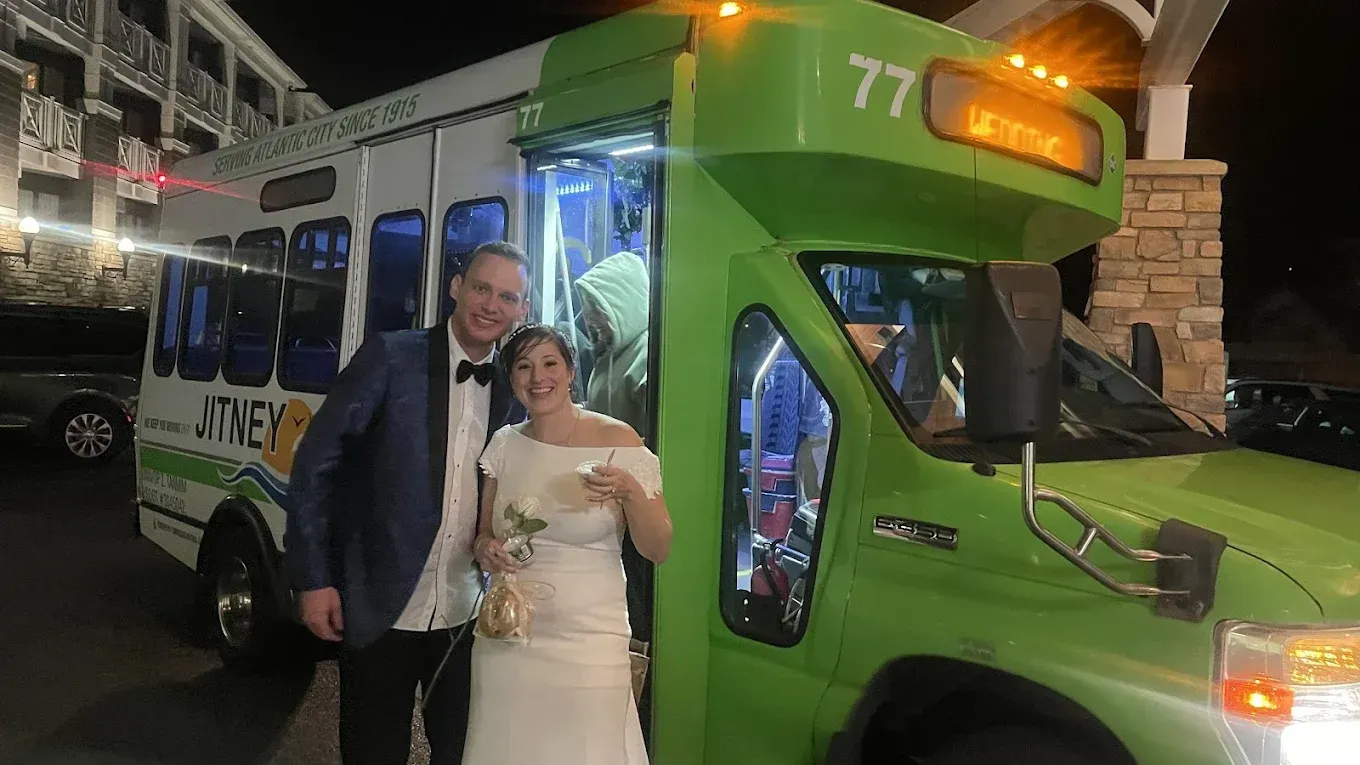 A bride and groom are standing in front of a green bus.