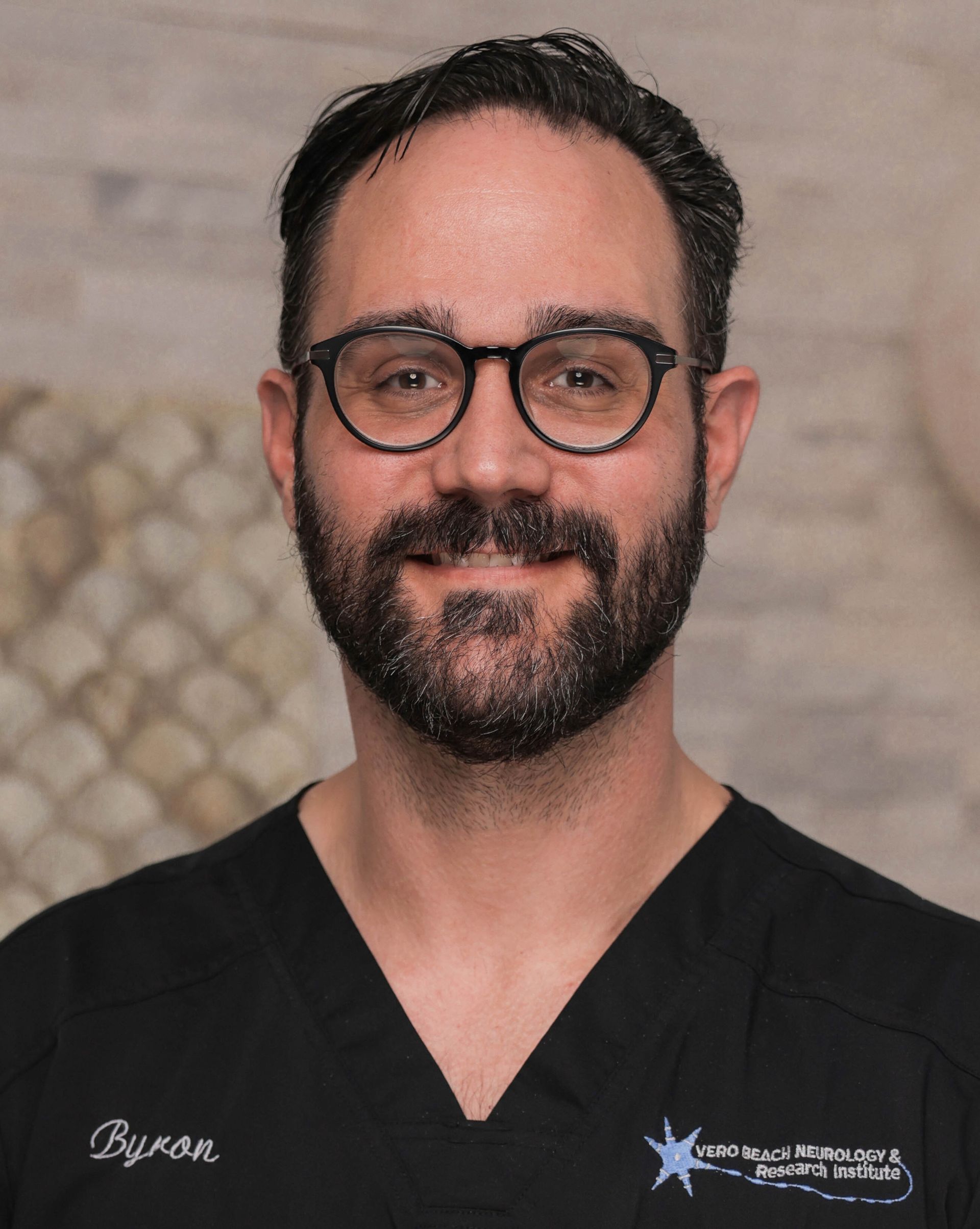 A man with a beard and glasses is wearing a black scrub top.