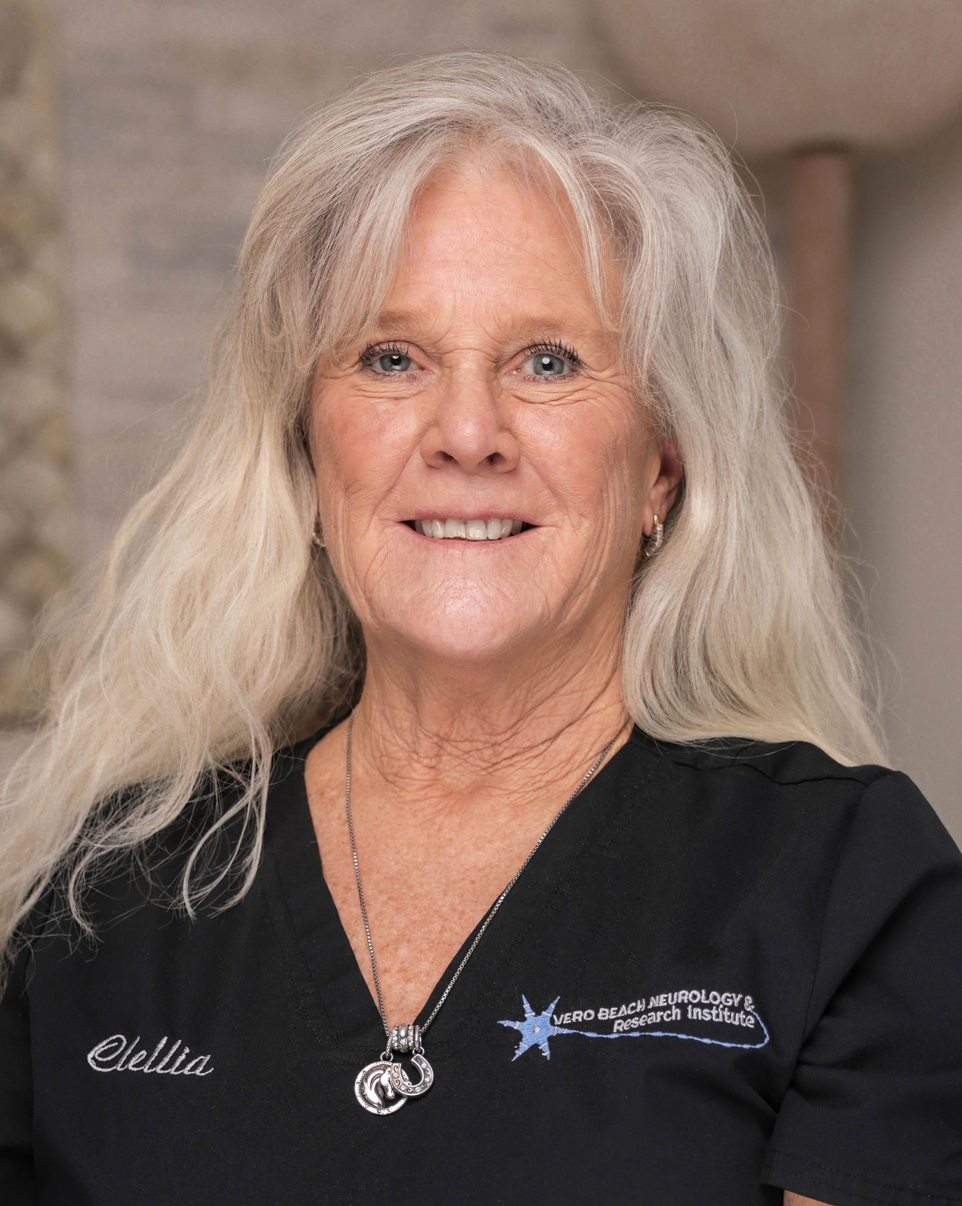 A woman wearing a black scrub top and a necklace is smiling for the camera.