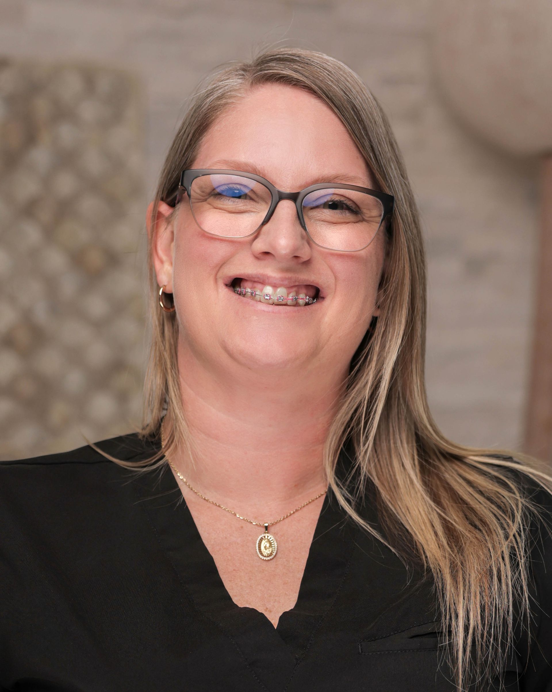 A woman wearing glasses and a necklace is smiling for the camera.