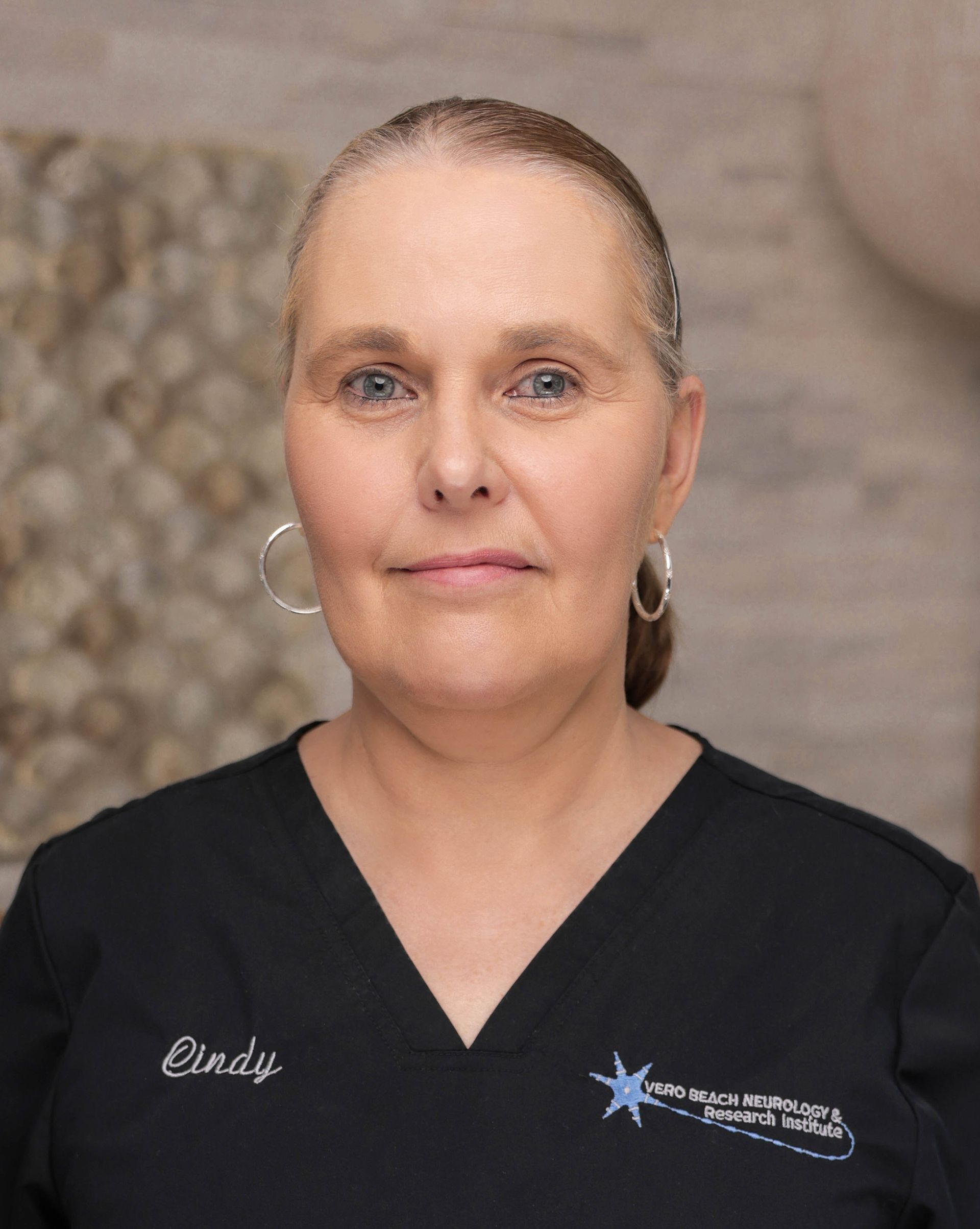 A woman is wearing a black scrub top and earrings.