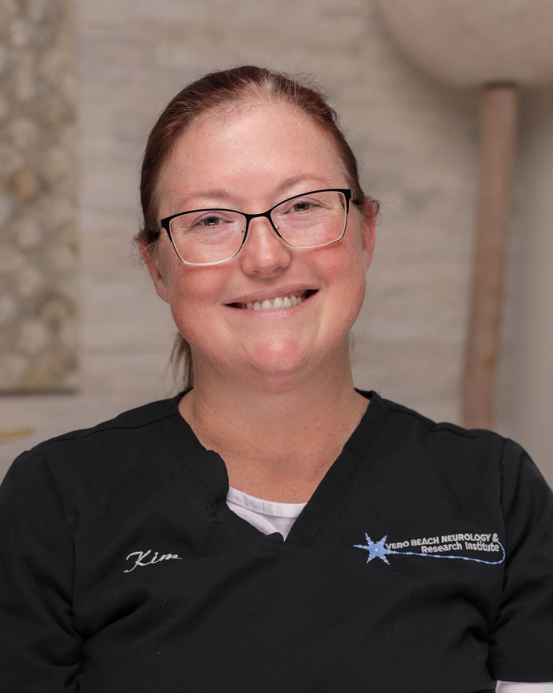 A woman wearing glasses and a black scrub top is smiling for the camera.
