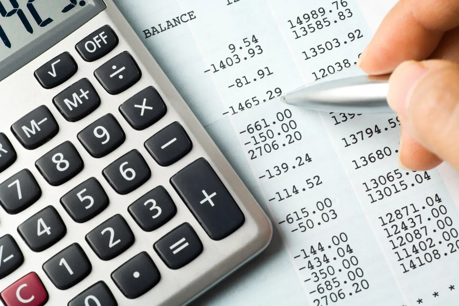 Calculator and hand with pen pointing at financial numbers on a printed document.