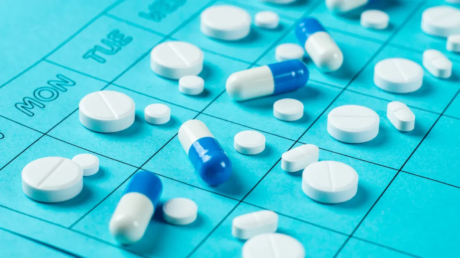 Pills and capsules scattered on a blue calendar, illustrating medication organization and scheduling.