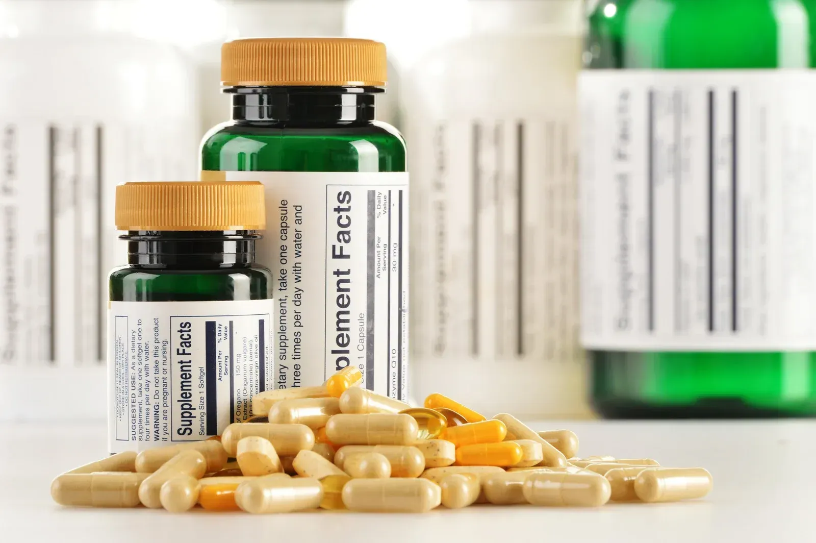 Pills spilling from jars with supplement facts labels. Green and white bottles, light brown pills.