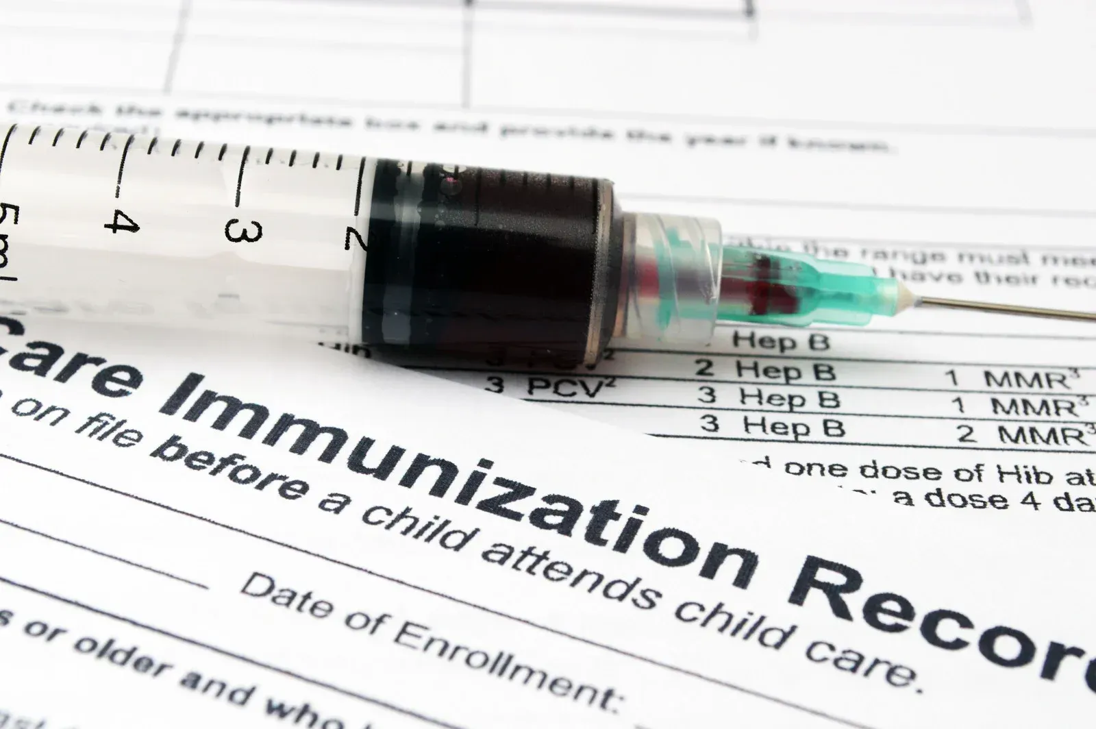 Syringe filled with liquid on top of a healthcare immunization record form.