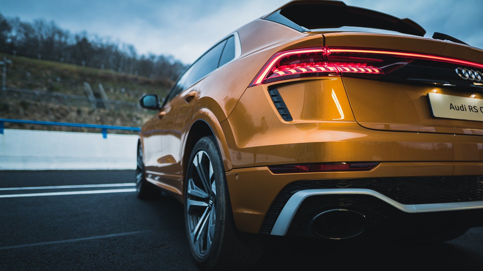 The rear end of a gold audi q8 is driving down a road.