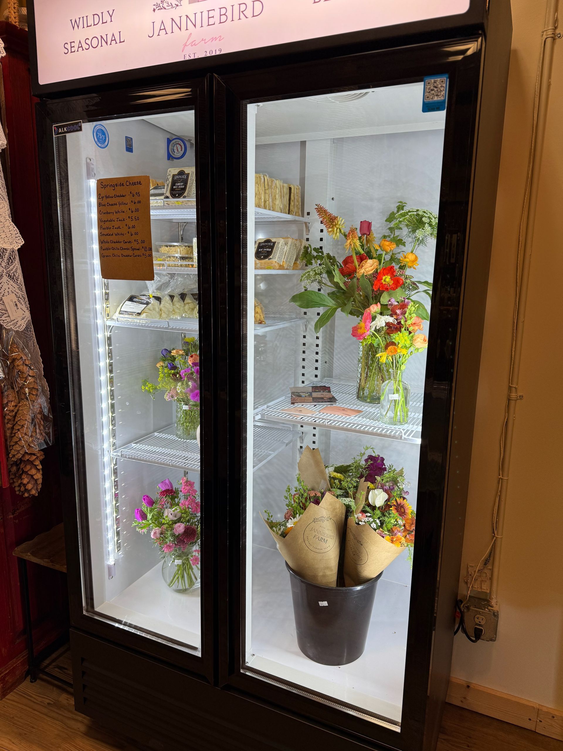 A refrigerator filled with vases of flowers and cakes.