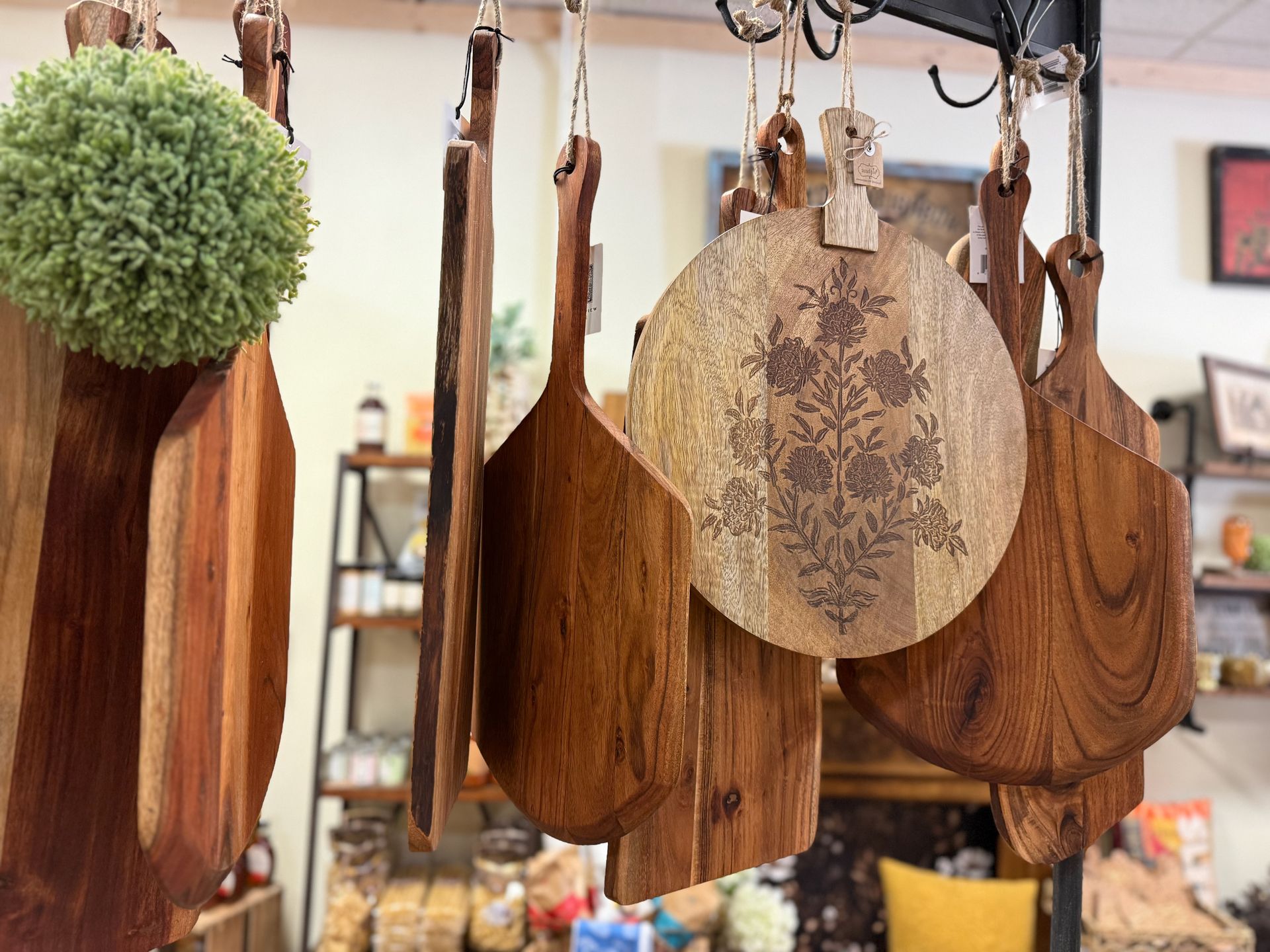 A bunch of wooden cutting boards are hanging from hooks in a store.