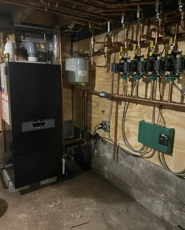 A boiler is sitting in a basement surrounded by pipes.