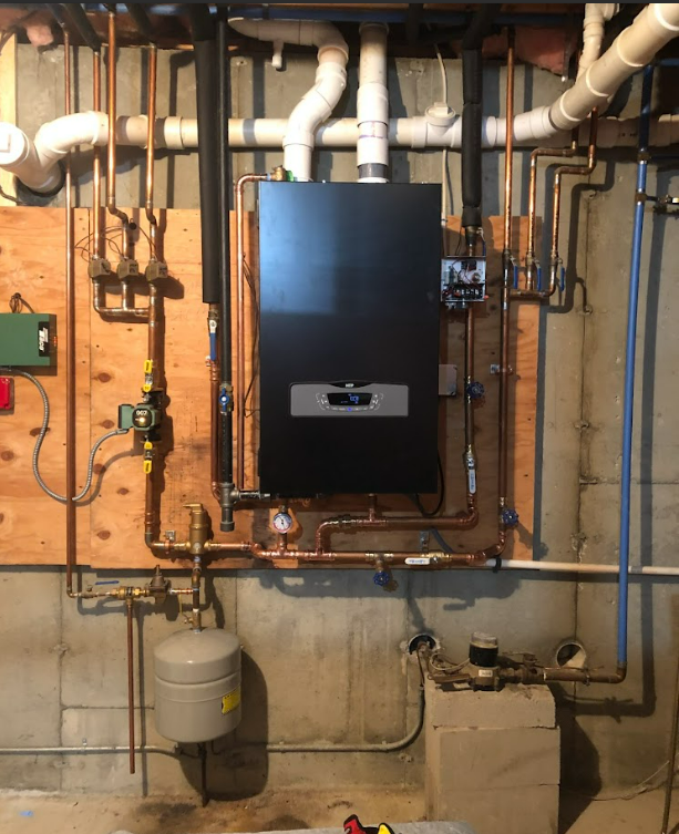 A black boiler is mounted to the wall in a basement