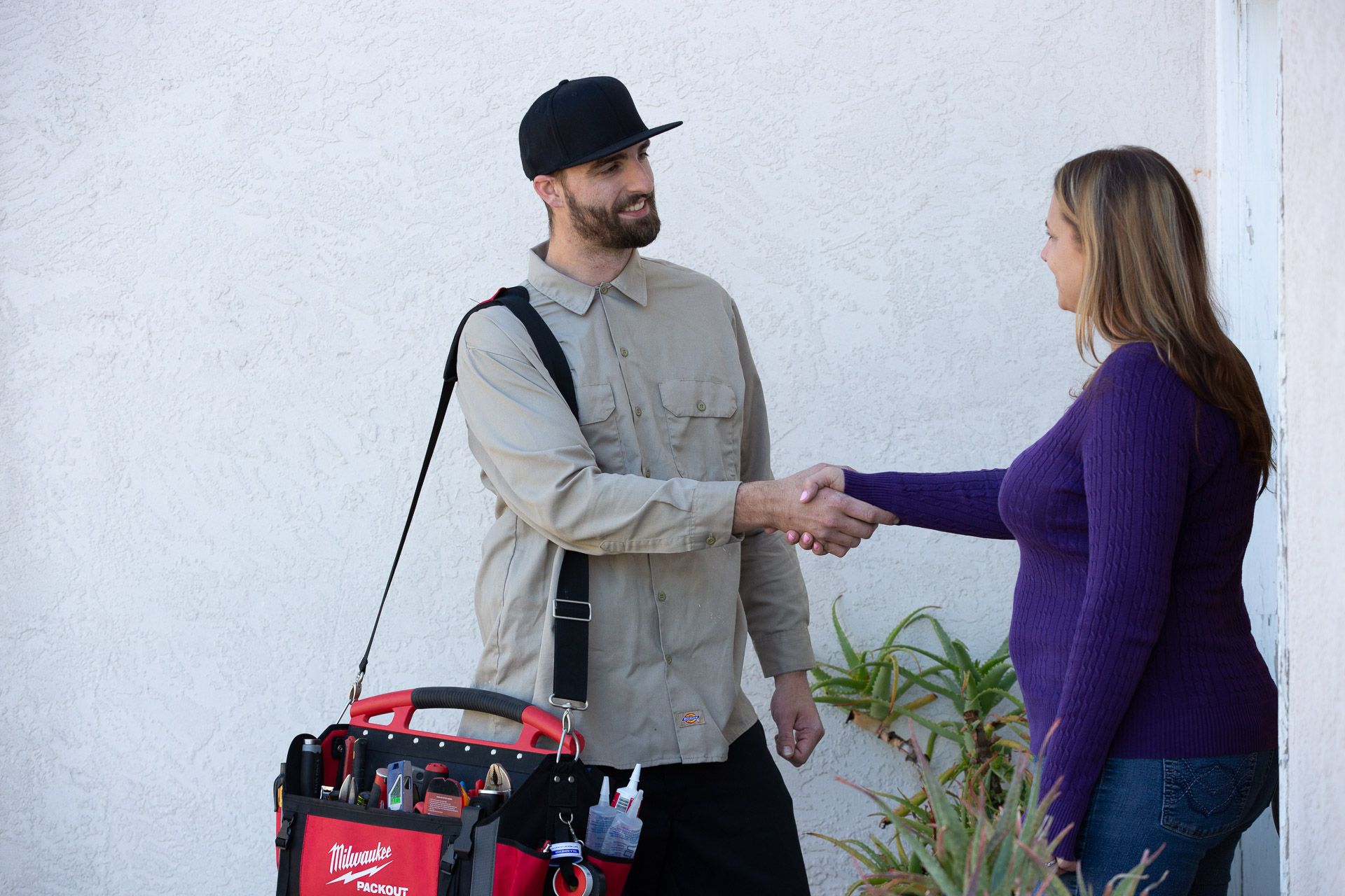 A man with a tool bag is shaking hands with a woman.