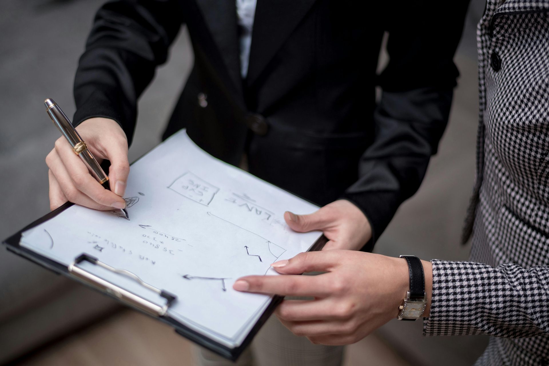 A woman is writing on a clipboard while another woman points at it.