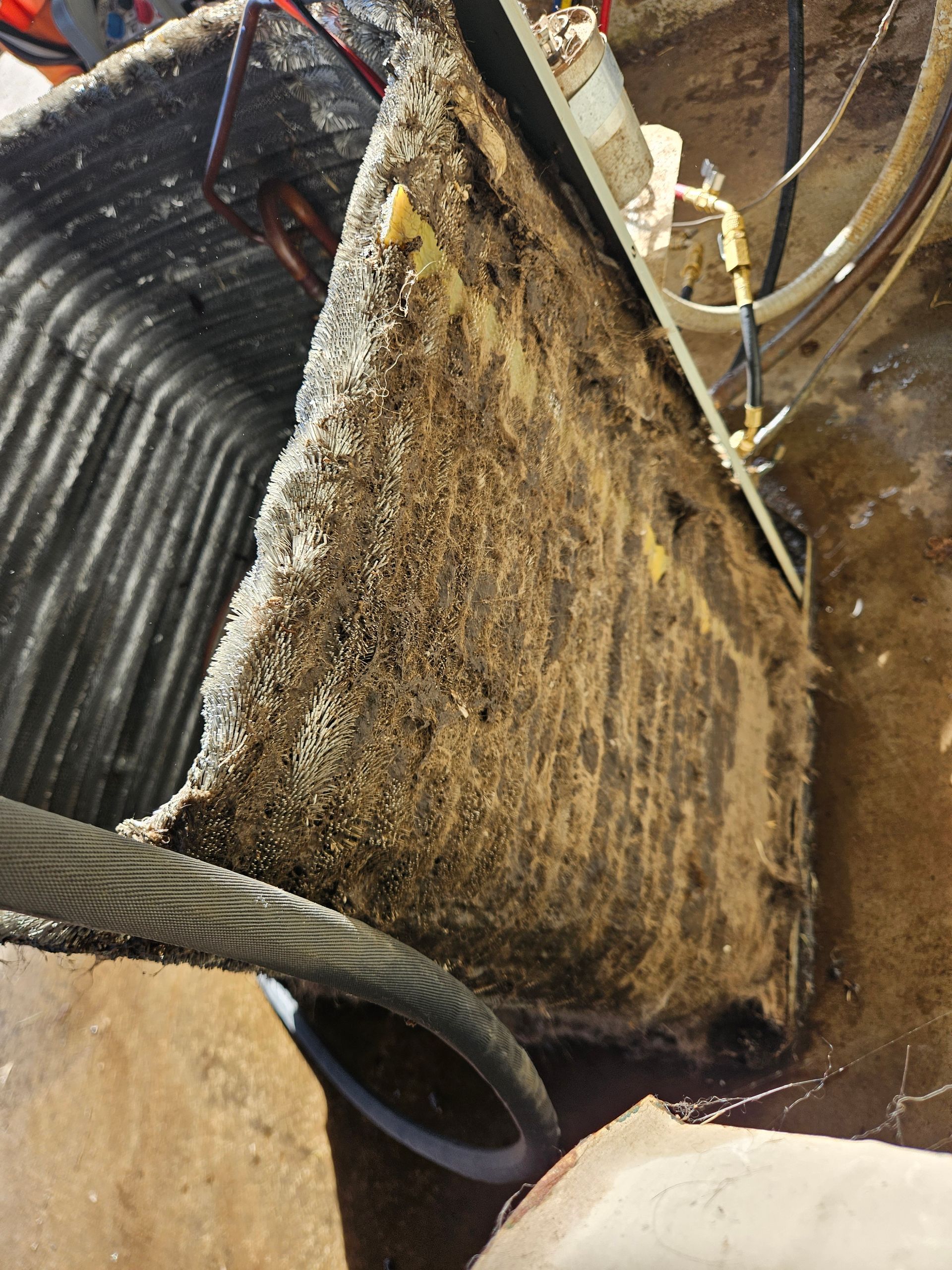 Clogged HVAC air handler filter covered in debris, next to cooling coils.