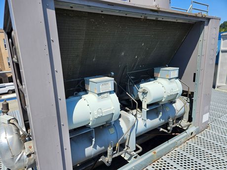 Two gray air conditioning compressors on a rooftop, viewed from the front.