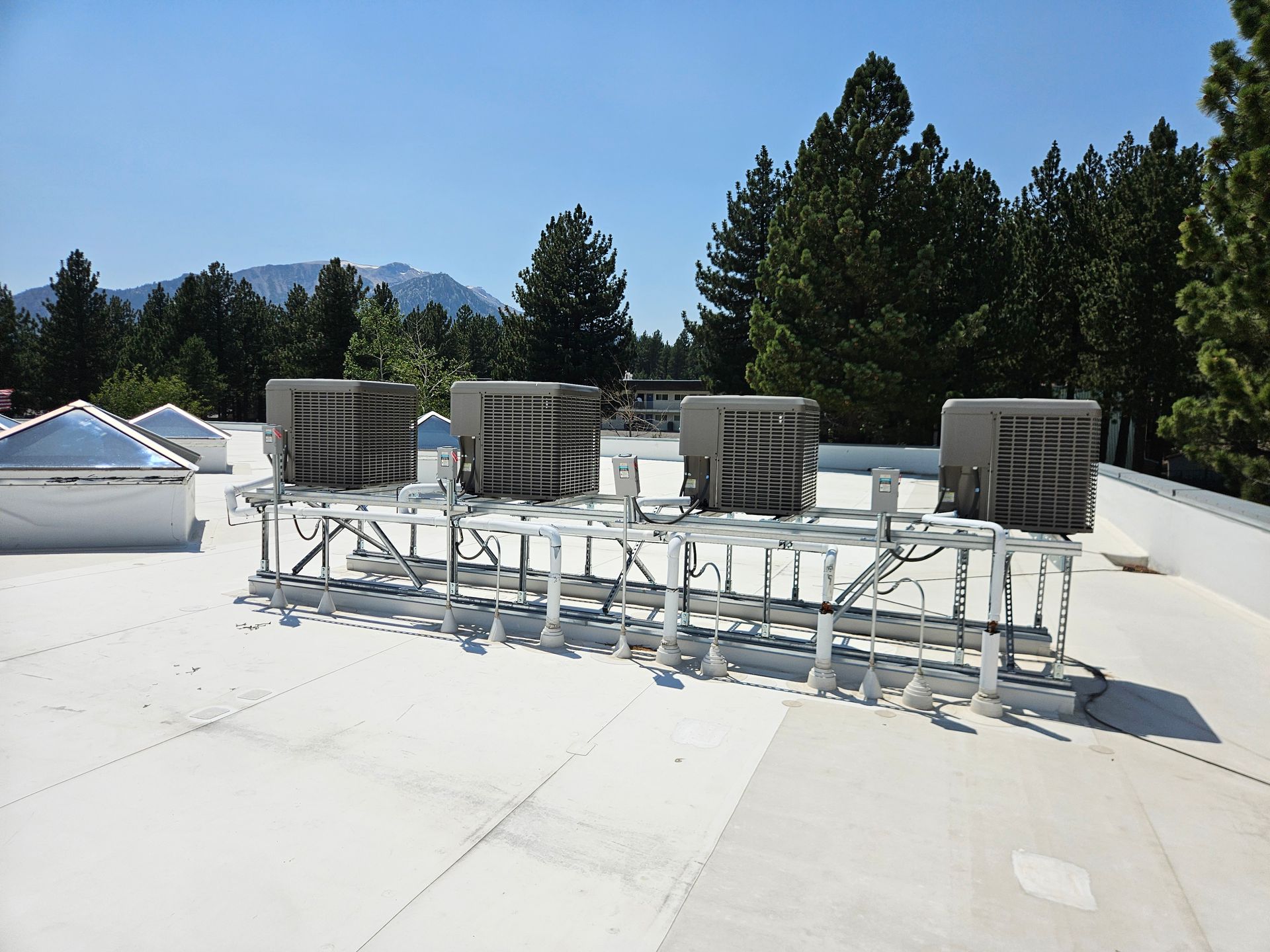 Rooftop with HVAC units and supporting framework. Trees and a mountain are in the background under a blue sky.