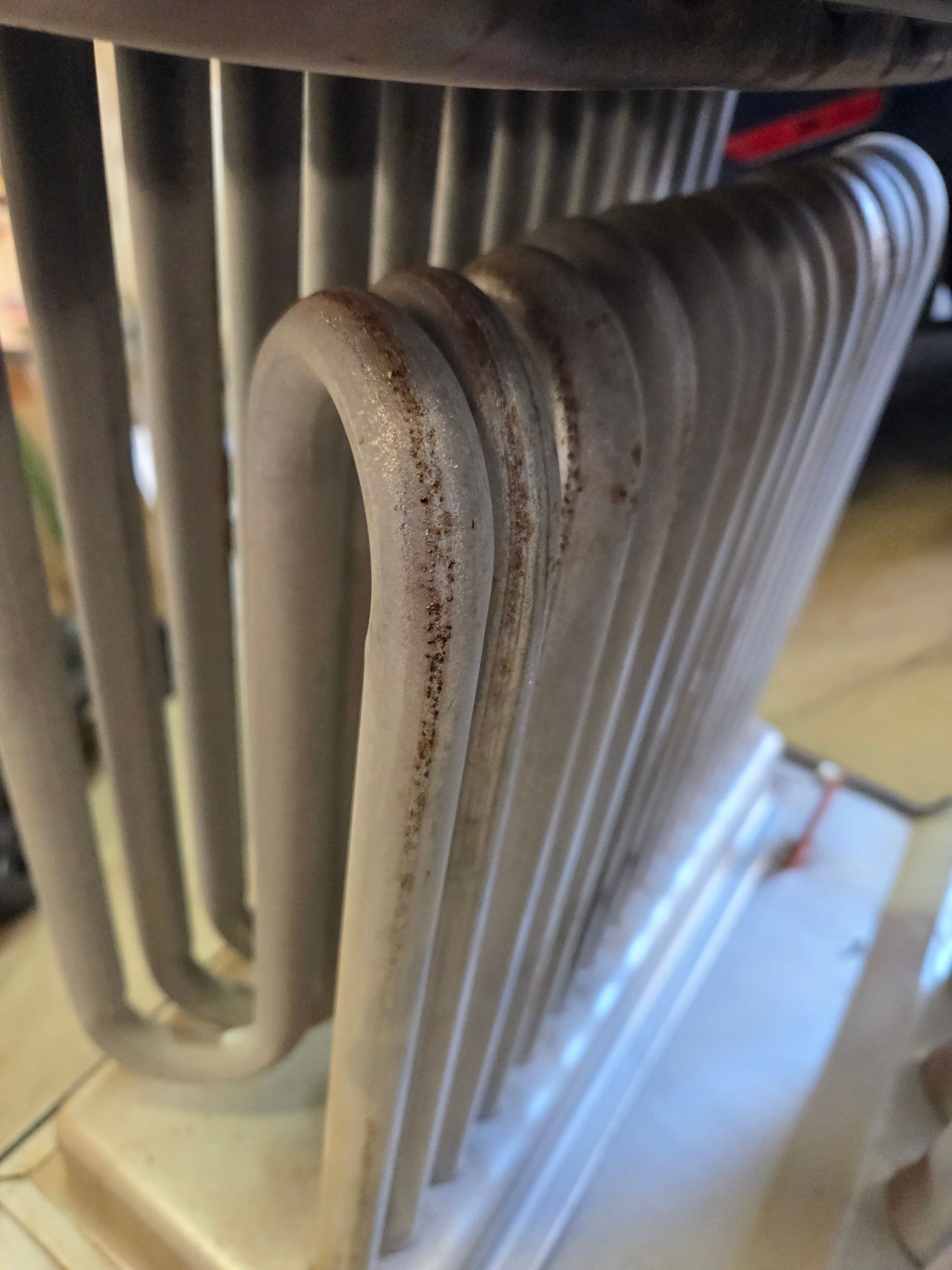 Close-up of a white, curved metal heat exchanger with rust-colored deposits.