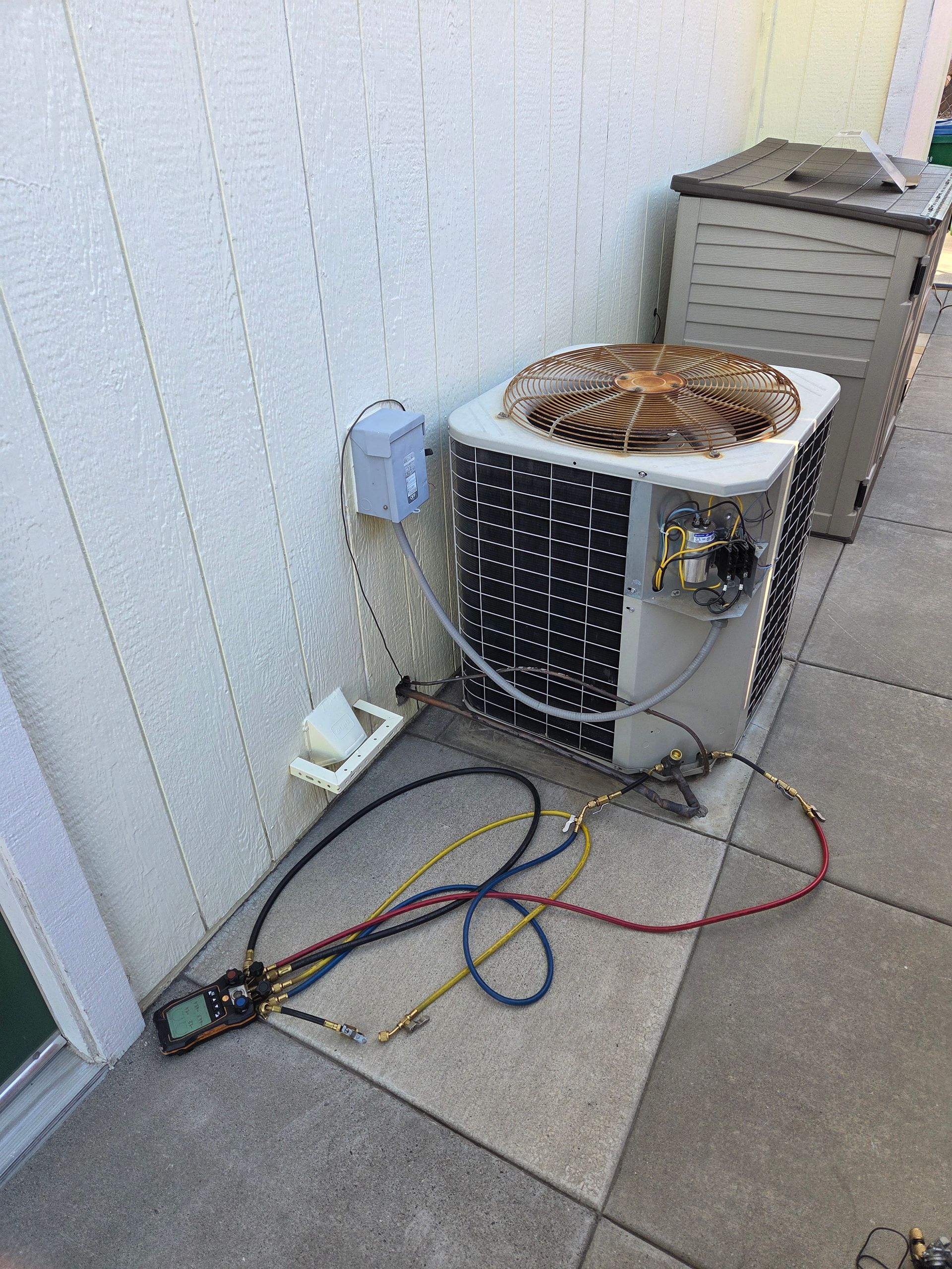 AC unit being serviced outdoors, with hoses connected to a gauge.