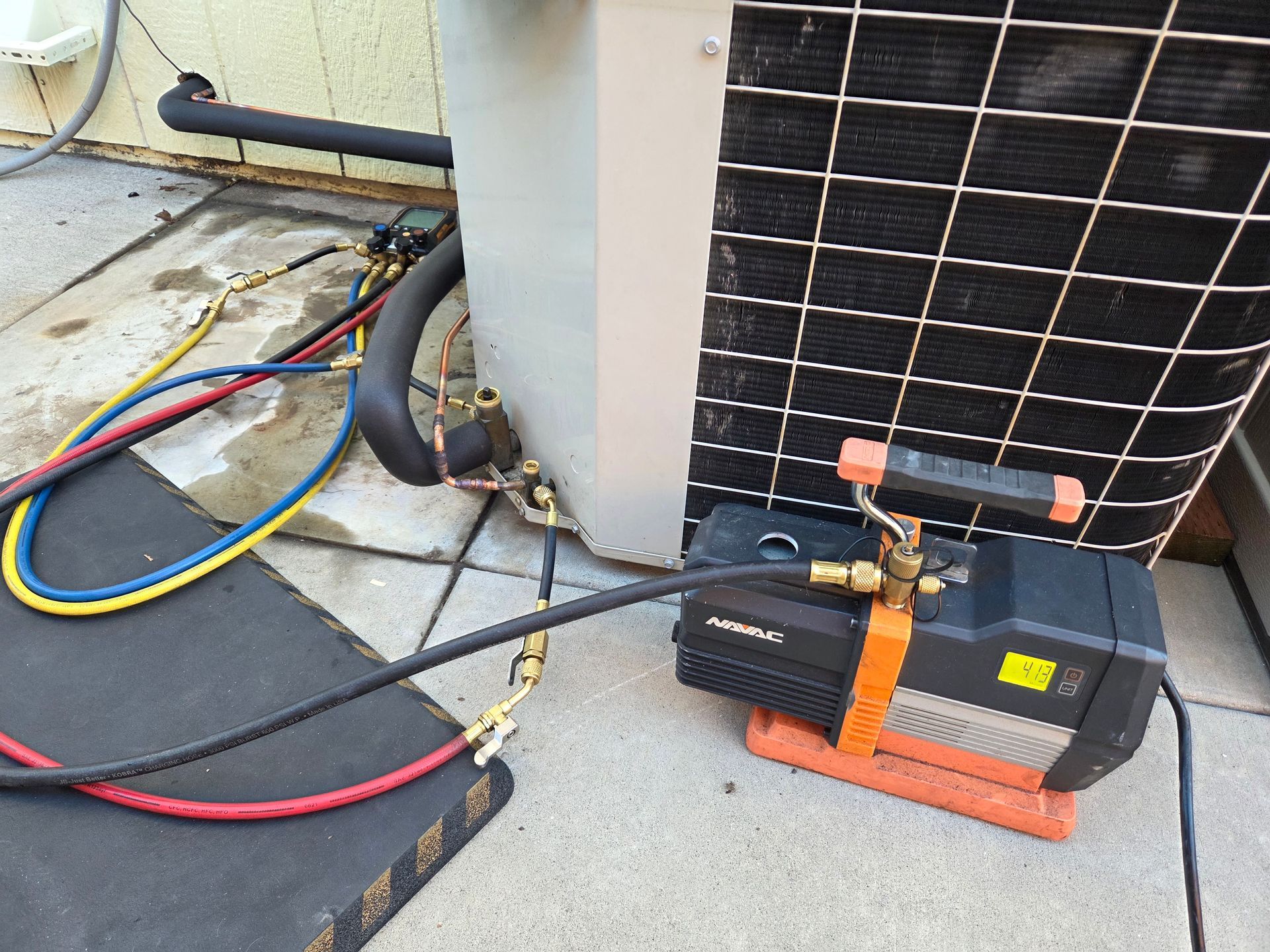 HVAC unit being serviced. Vacuum pump attached with hoses; black, gray, and copper pipes.