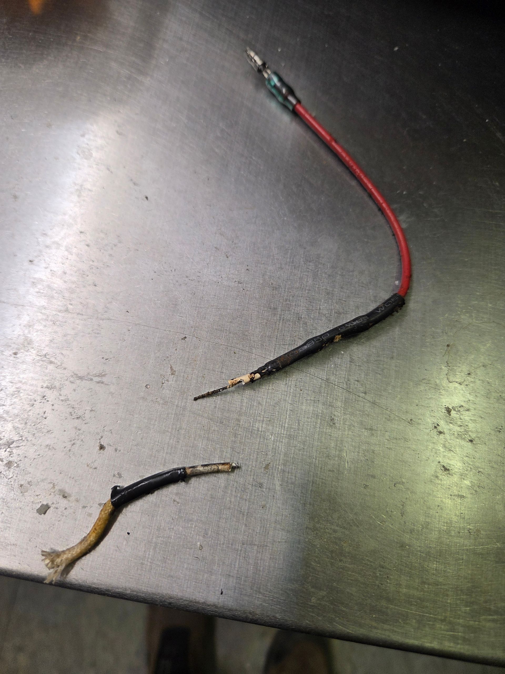 Broken electrical wire with red and black insulation, lying on a metallic surface.