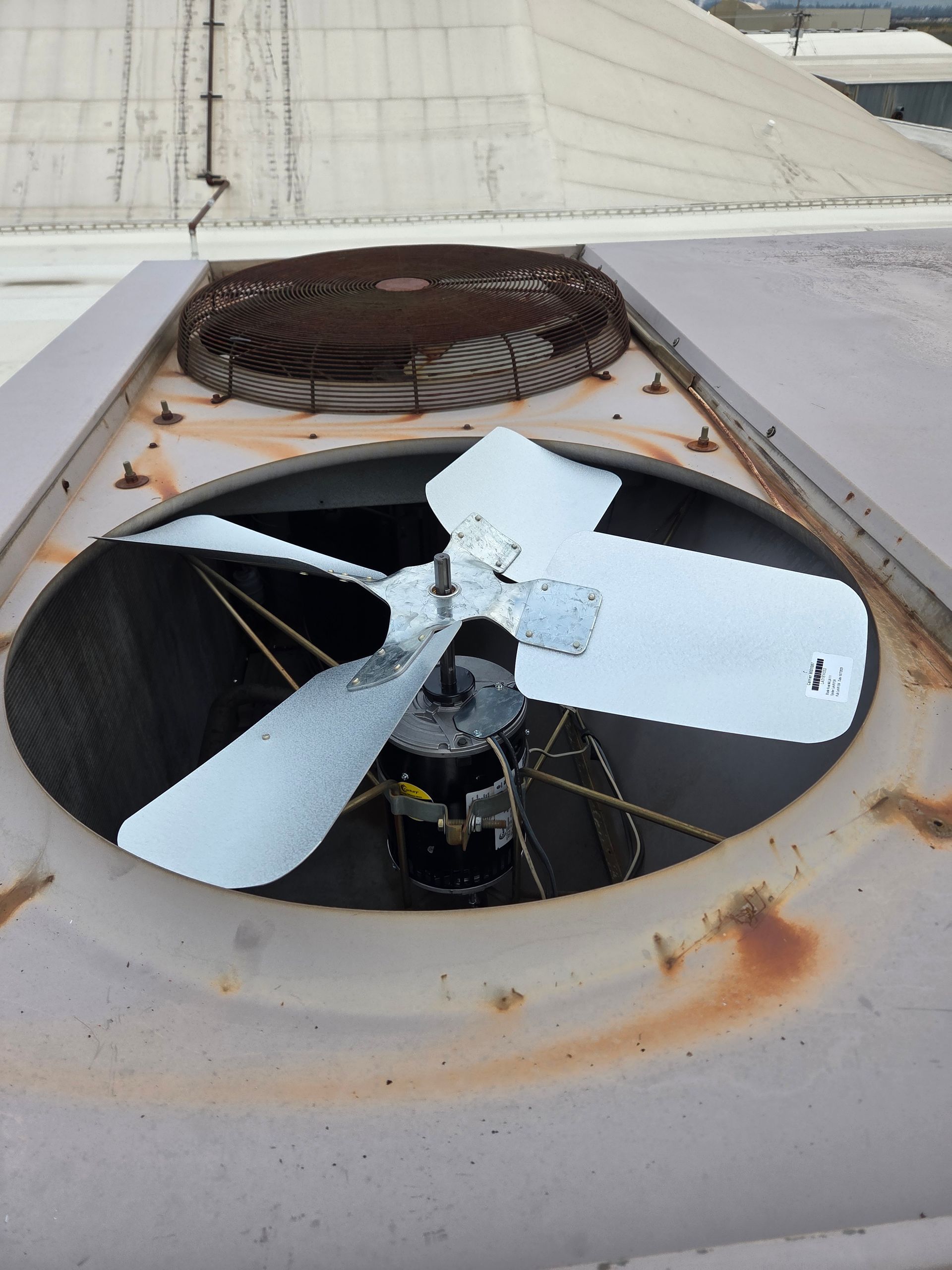 Overhead view of a rooftop air conditioning unit with a fan and rusted metal components.