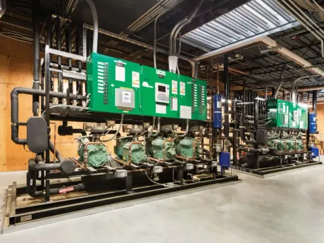 Industrial refrigeration equipment with green control panels, pipes, and compressors in a warehouse.