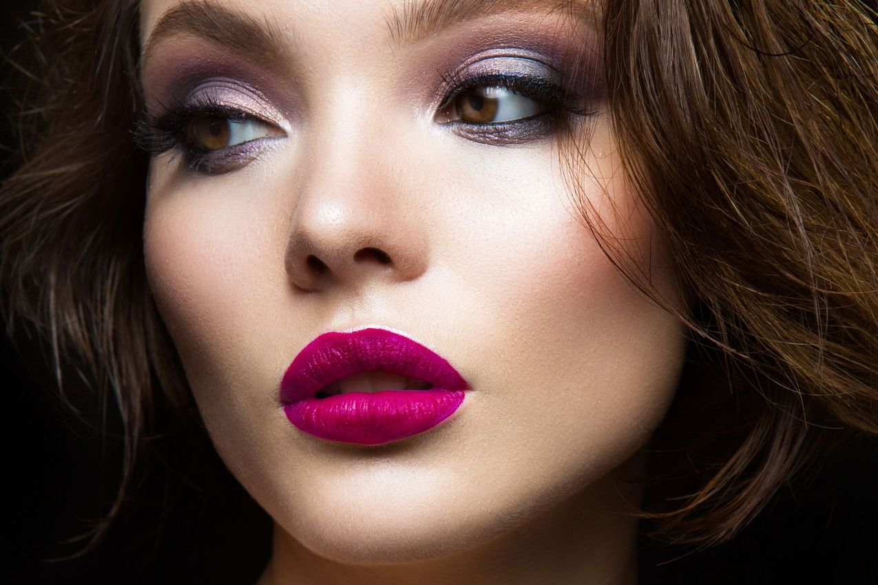 Ritratto ravvicinato di una donna con un trucco occhi intenso e un rossetto color magenta acceso.