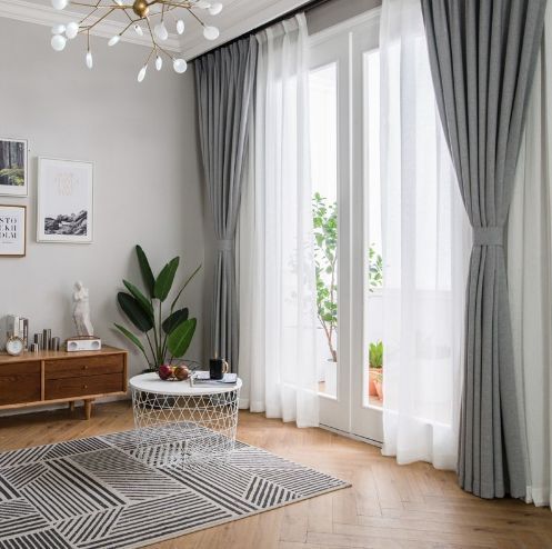 Una sala de estar con una mesa, alfombra, cortinas y una lámpara de araña.