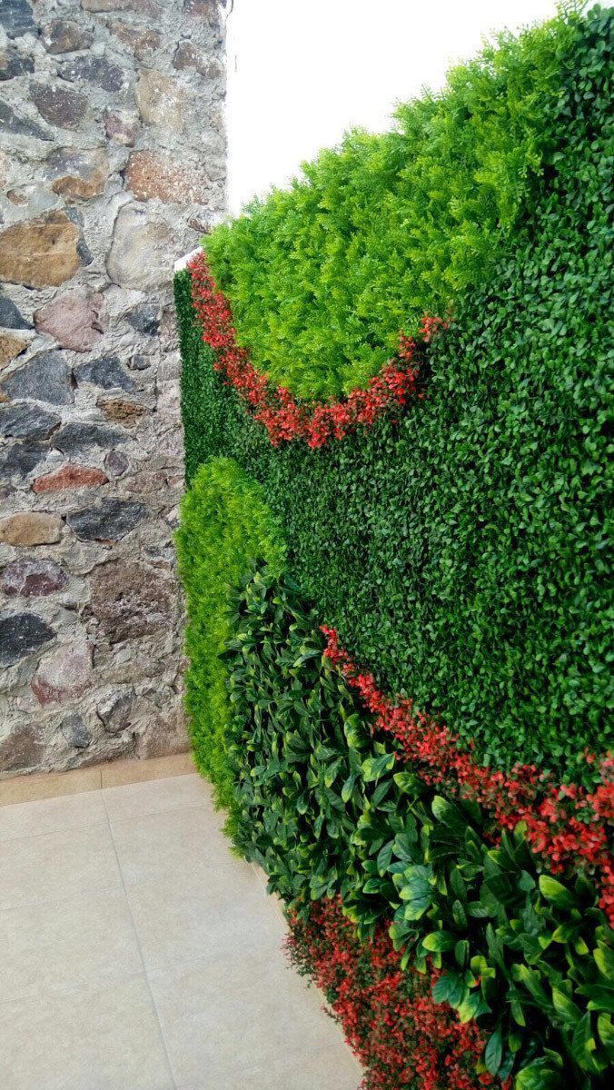 Una pared verde con flores rojas delante de un muro de piedra.