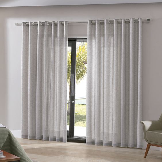 Una sala de estar con una puerta corrediza de vidrio y cortinas blancas.