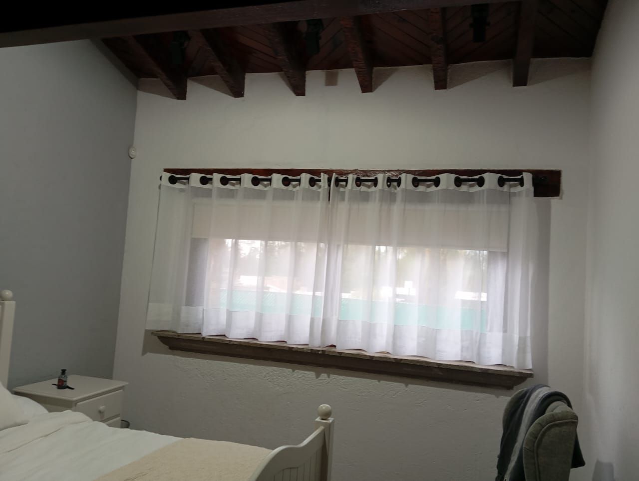 Un dormitorio con una cama y una ventana con cortinas blancas.
