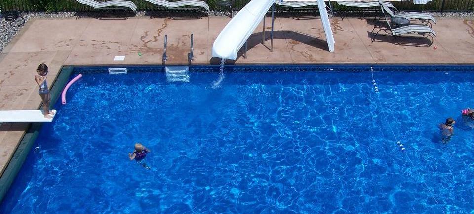 A group of people are swimming in a large swimming pool with a slide.