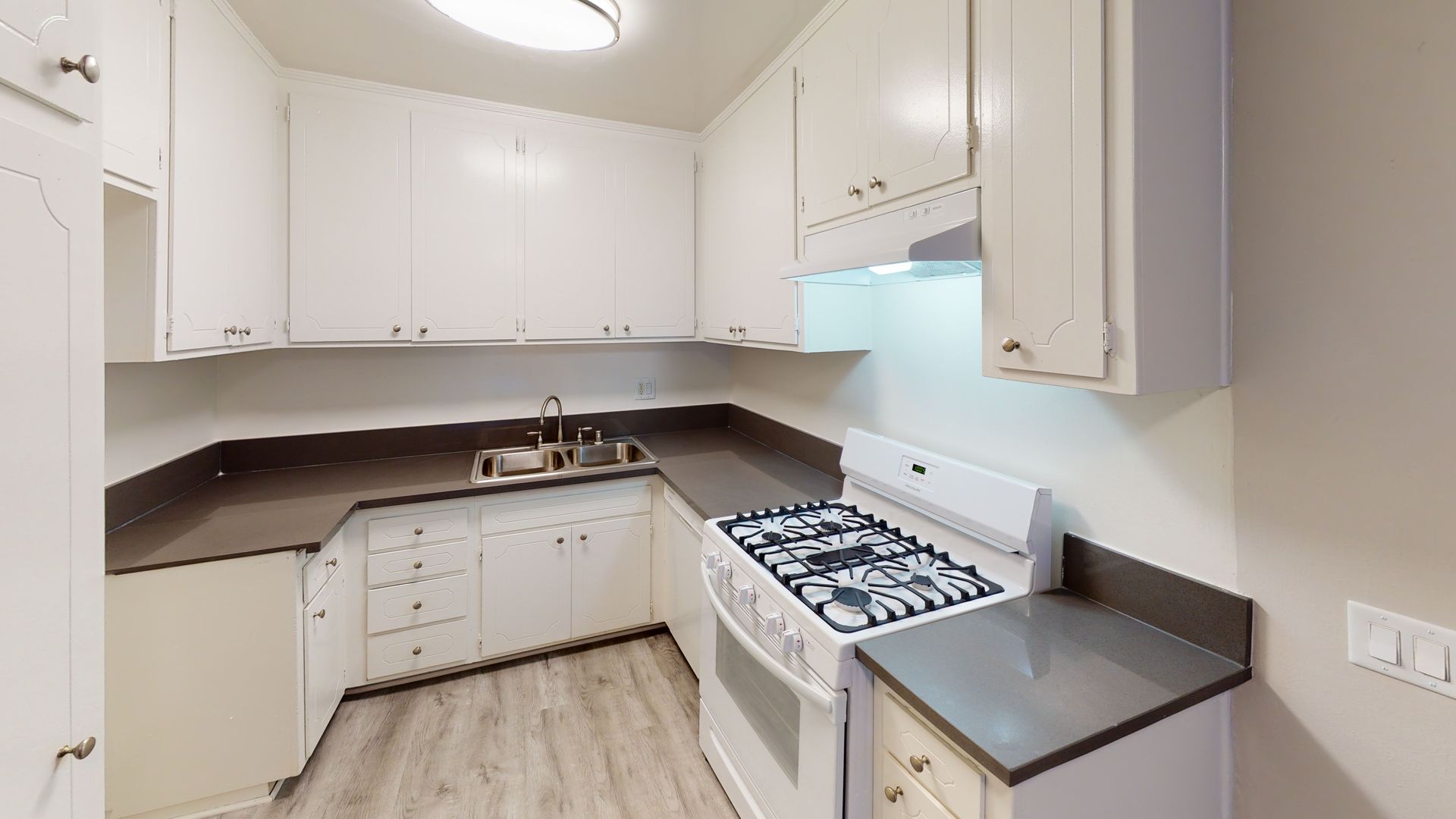 White kitchen with cabinets, stove, sink, and gray countertops.