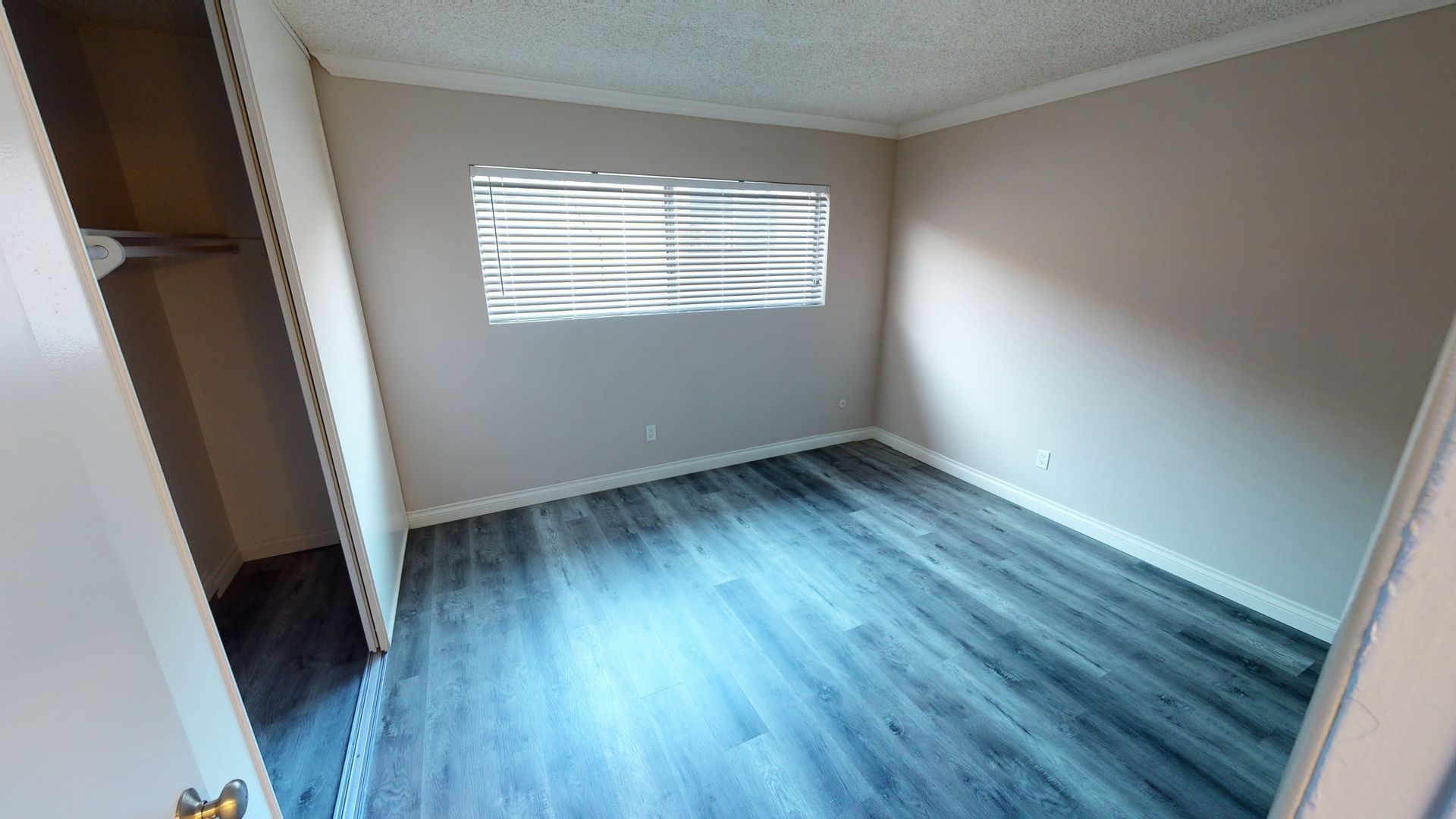 Empty room with wood-look flooring, a window with blinds, and a closet.