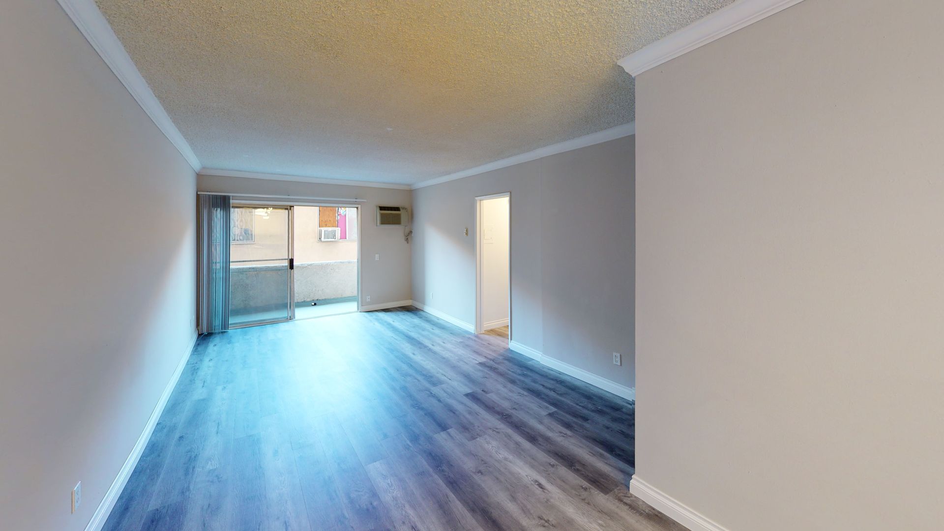 Interior view of a room with wood-like flooring, white trim, and a doorway to a balcony and another room.